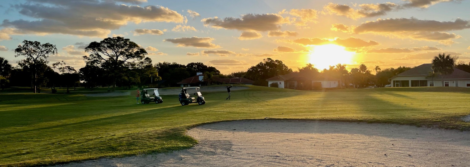 Golf course at sunset with two golf carts and a player swinging a club in the background.
